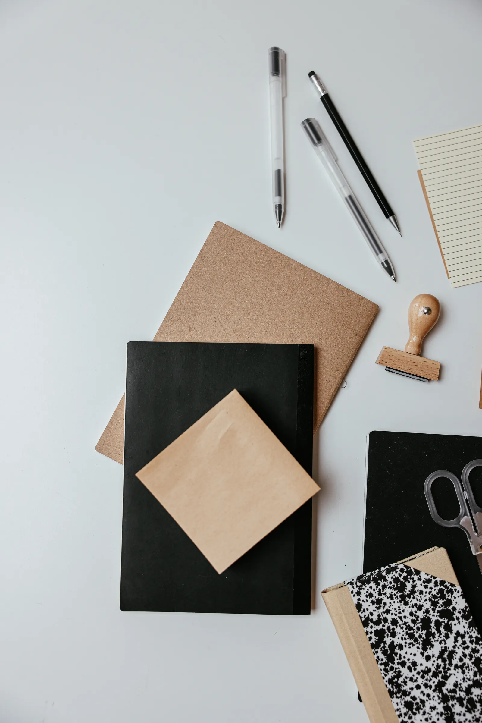 Pens, a pencil, notebooks and paper stationery arranged on a light desk